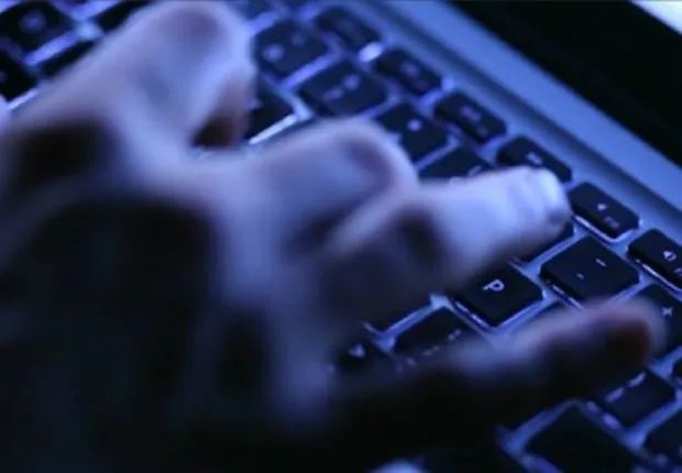 Mãos digitando em um teclado sob luz azulada, ilustrando ataques coordenados por botnets