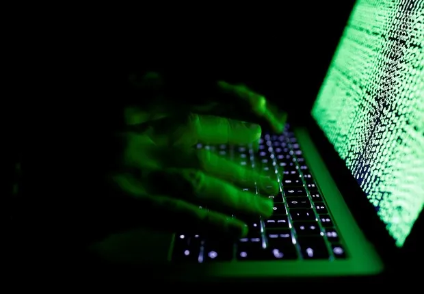 Mãos sobre um teclado iluminadas pela luz verde de uma tela coberta de código